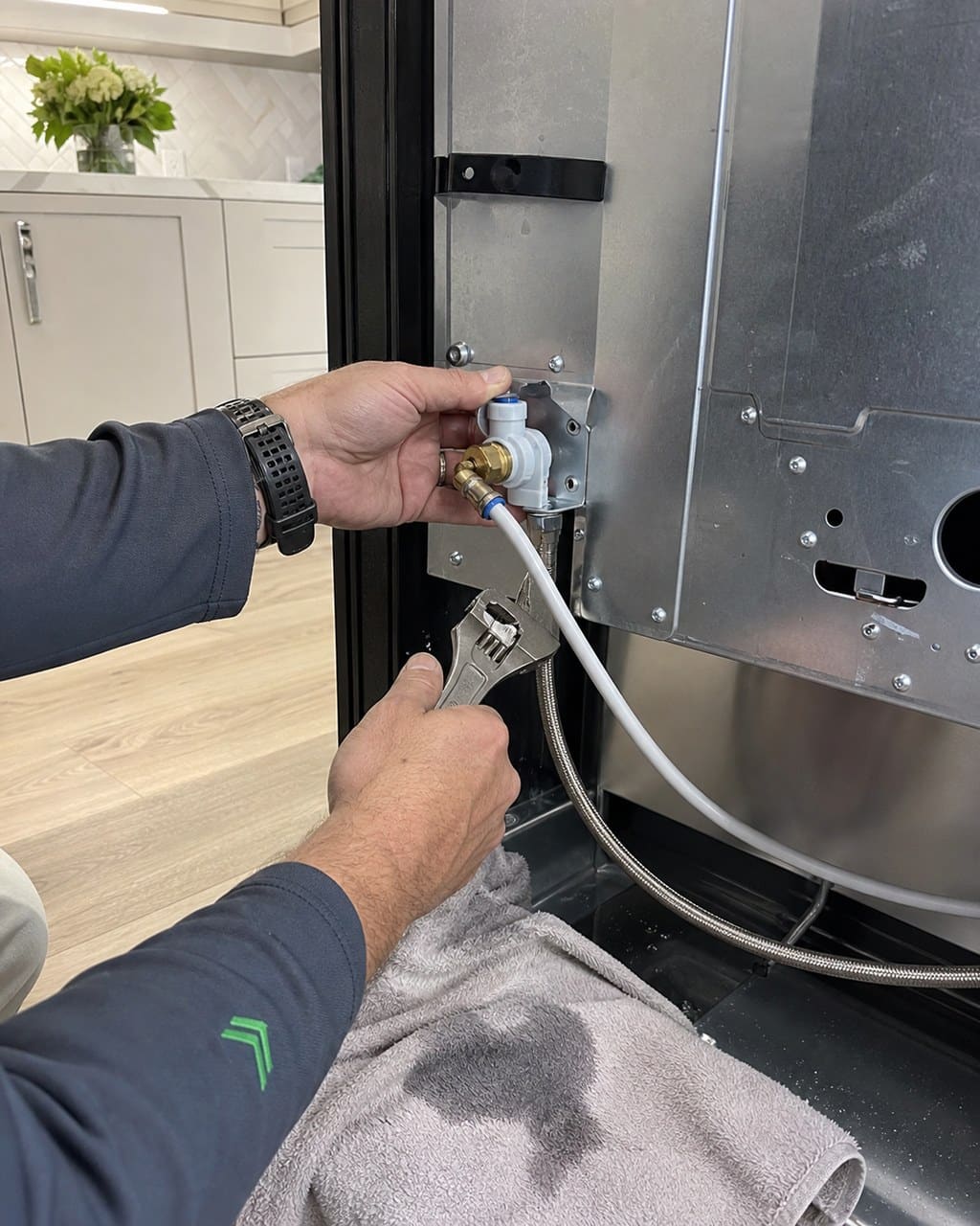Technician replacing the water inlet valve behind a built-in Sub-Zero refrigerator in a Dublin kitchen